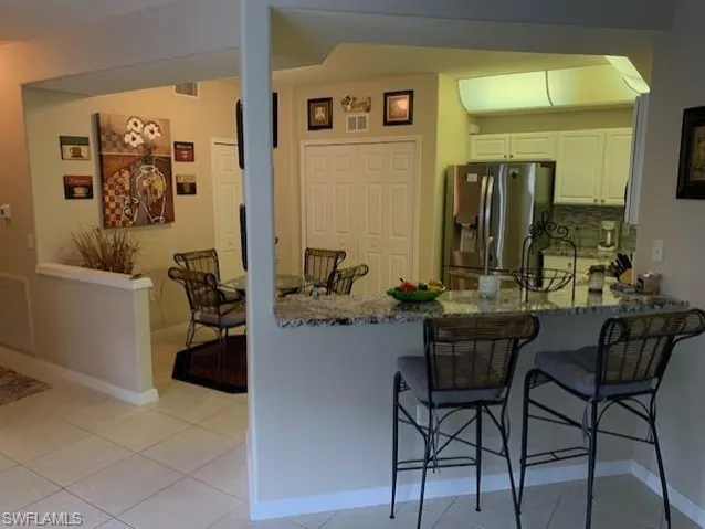 Kitchen featuring stainless steel fridge, dark stone countertops, a peninsula, and a breakfast bar area