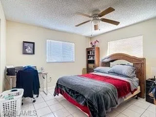 Bedroom with light tile patterned floors, ceiling fan, and a textured ceiling