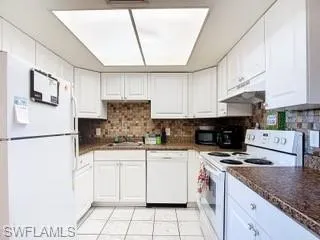 Kitchen with white appliances, dark countertops, and white cabinets
