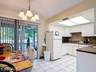 Kitchen featuring dark countertops, freestanding refrigerator, a chandelier, backsplash, and white cabinetry