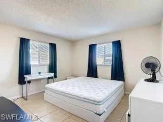 Bedroom with light tile patterned floors, a textured ceiling, and multiple windows