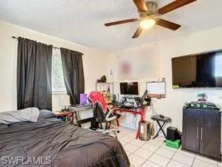Bedroom with a textured ceiling, a ceiling fan, and light tile patterned floors
