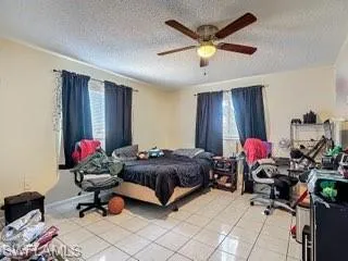 Bedroom with light tile patterned floors, a ceiling fan, and a textured ceiling