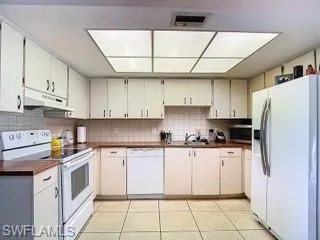 Kitchen with white appliances, light tile patterned flooring, and backsplash