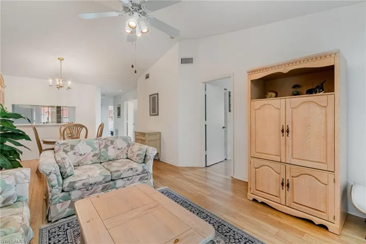 Living area featuring lofted ceiling, light wood-style floors, a chandelier, and ceiling fan