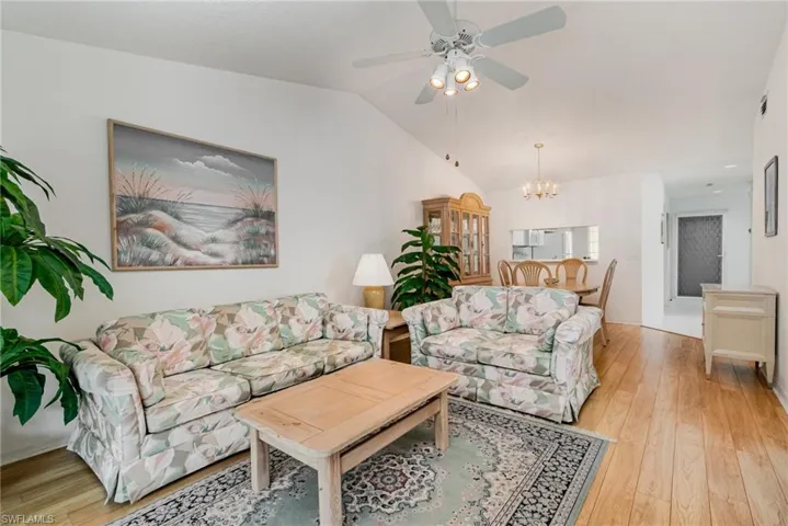 Living room with a chandelier, light wood-style flooring, vaulted ceiling, and a ceiling fan