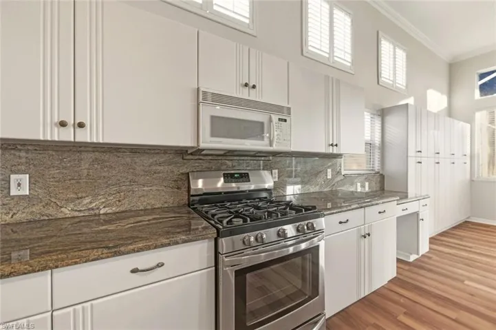 New Gas Kenmore Stove Kitchen with stainless steel gas range oven, white cabinets, ornamental molding, white microwave, and light wood-style flooring