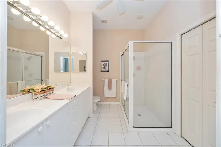 Bathroom featuring double vanity, a stall shower, light tile patterned floors, and ceiling fan
