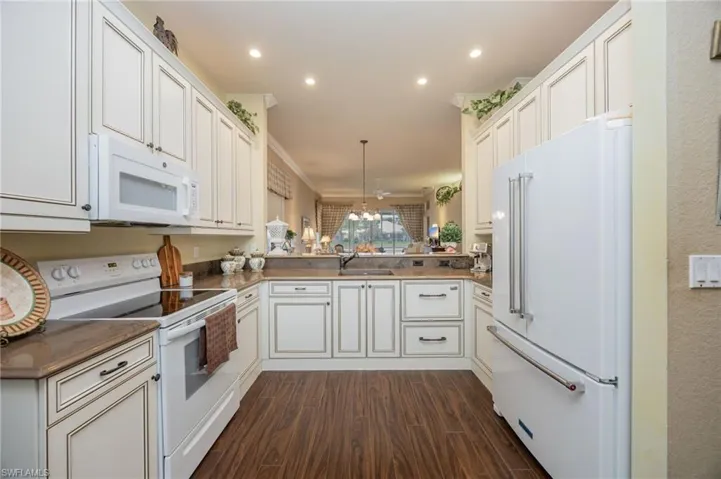 Kitchen with white appliances, white cabinetry, dark wood-style flooring, light stone counters, and ornamental molding