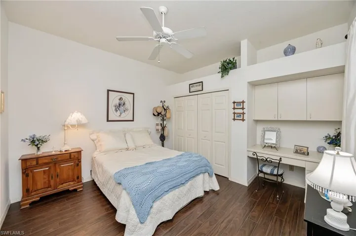 Bedroom with built in desk, dark wood-style floors, ceiling fan, and a closet