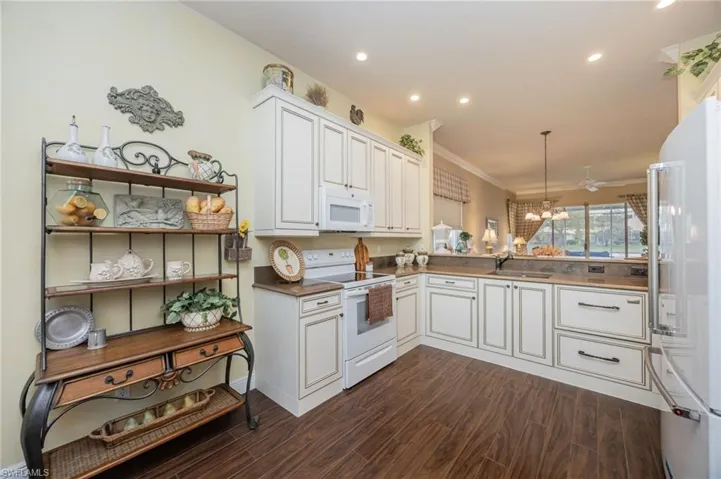Kitchen featuring white appliances, decorative light fixtures, dark wood-style floors, white cabinetry, and ornamental molding