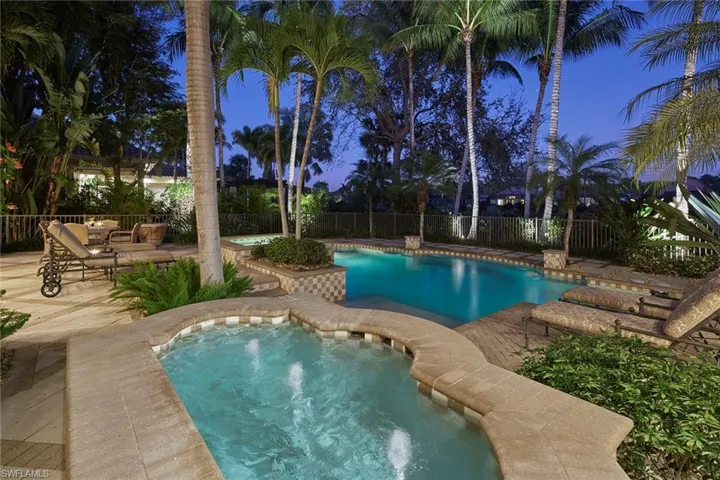 Pool at night with a patio, a fenced backyard, and a hot tub