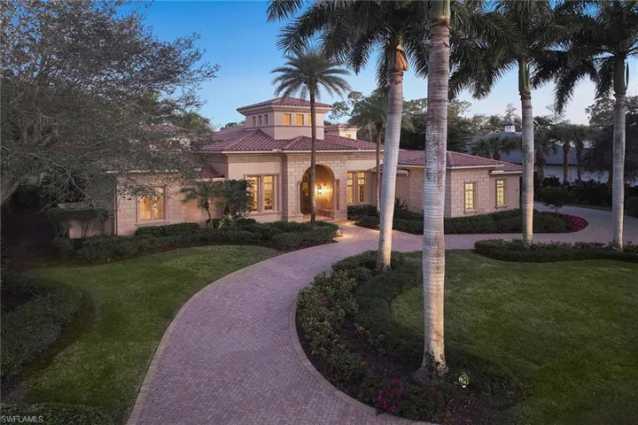 Mediterranean / spanish home featuring a tiled roof, a lawn, curved driveway, and stucco siding