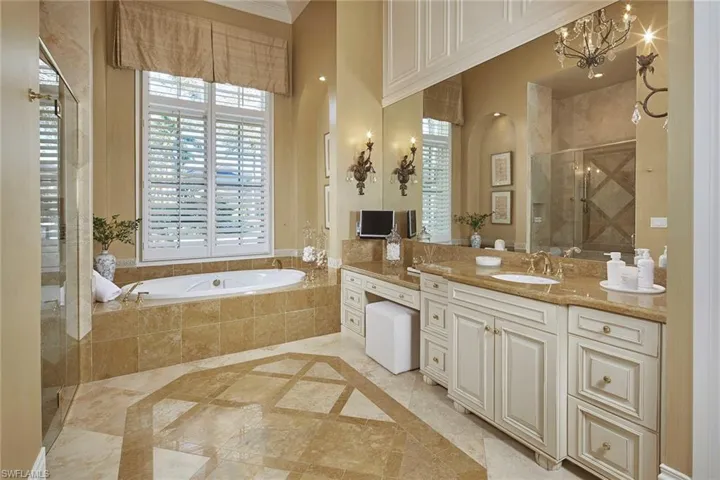 Full bathroom featuring a shower stall, vanity, a garden tub, inlaid floor details, and a chandelier
