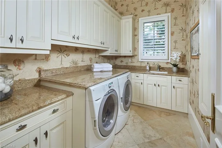 Laundry room featuring wallpapered walls, washing machine and clothes dryer, and cabinet space
