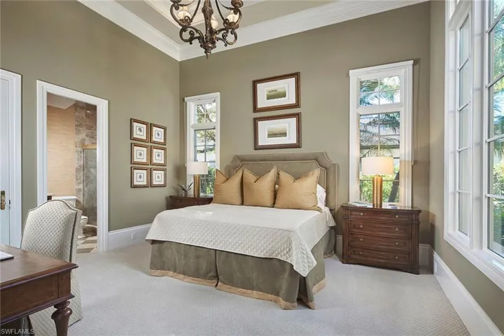 Carpeted bedroom featuring a chandelier, ensuite bathroom, and ornamental molding