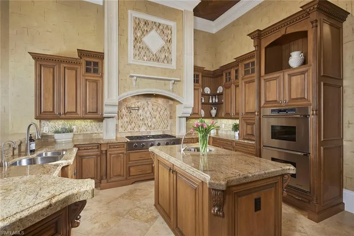 Kitchen featuring brown cabinets, appliances with stainless steel finishes, light stone countertops, ornamental molding, and a high ceiling