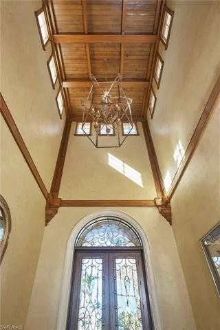Entrance foyer with a towering ceiling, a wooden ceiling with exposed beams, a textured wall, and french doors