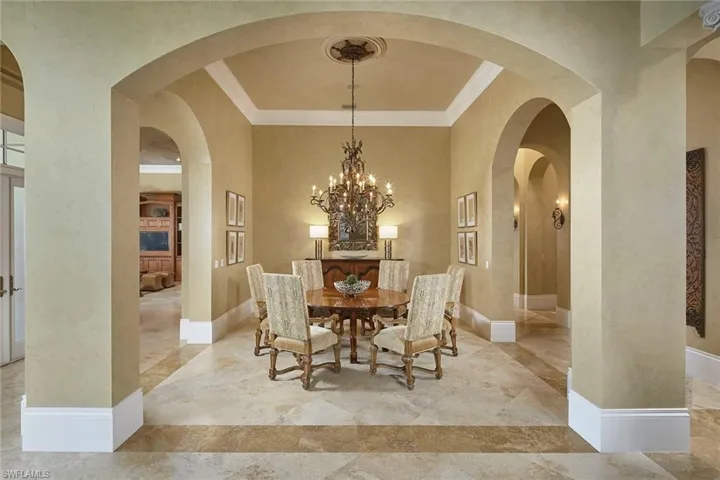 Dining room with crown molding, a chandelier, arched walkways, and a textured wall