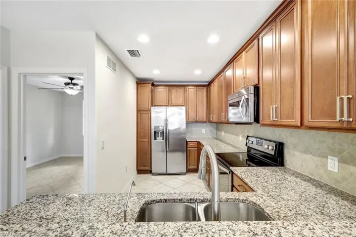 Kitchen with sink, light tile patterned floors, stainless steel appliances, light stone countertops, and decorative backsplash