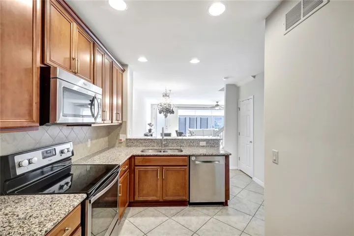 Kitchen with appliances with stainless steel finishes, tasteful backsplash, sink, light tile patterned floors, and light stone countertops