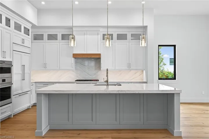 Kitchen featuring glass fronted cabinets, light counters, decorative light fixtures, and wood finished floors