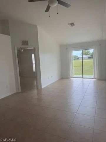 Empty room featuring healthy amount of natural light, light tile patterned floors, a ceiling fan, and lofted ceiling