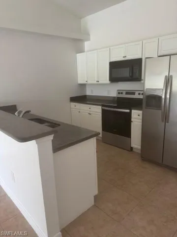 Kitchen featuring dark countertops, refrigerator, range, and white cabinetry