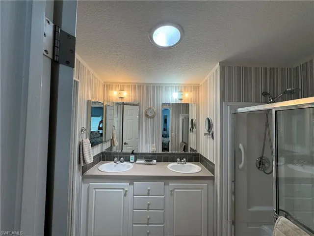Ensuite bathroom with a textured ceiling, ensuite bath, a sink, and a stall shower