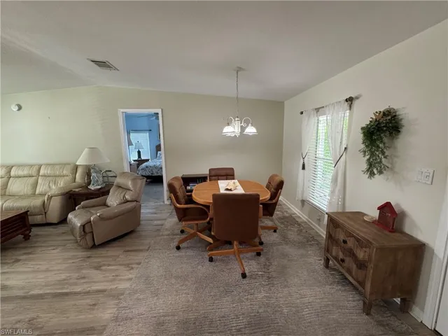 Dining room featuring a chandelier, wood finished floors, visible vents, baseboards, and vaulted ceiling