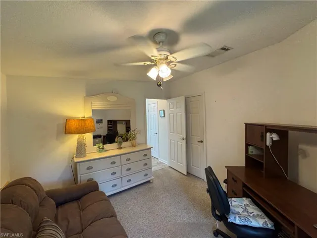 Home office featuring light carpet, a textured ceiling, visible vents, and a ceiling fan