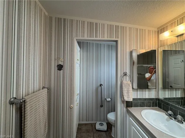Bathroom featuring vanity, a textured ceiling, toilet, and wallpapered walls