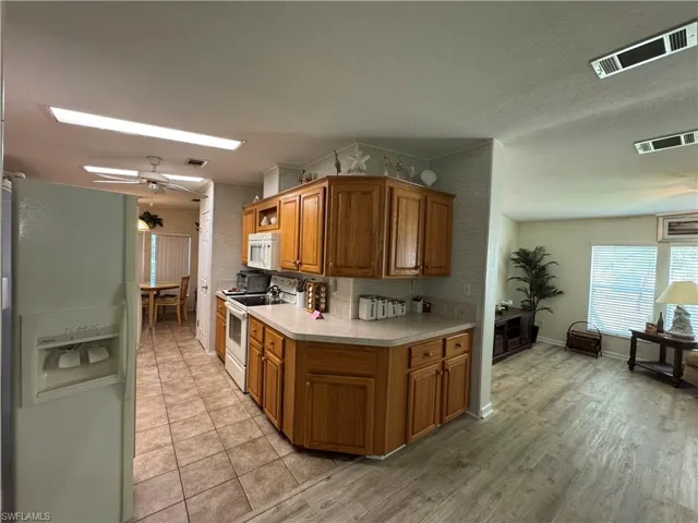 Kitchen featuring light countertops, white appliances, brown cabinetry, and visible vents