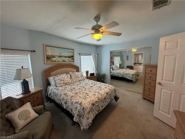 Bedroom featuring light carpet, a textured ceiling, visible vents, and a ceiling fan