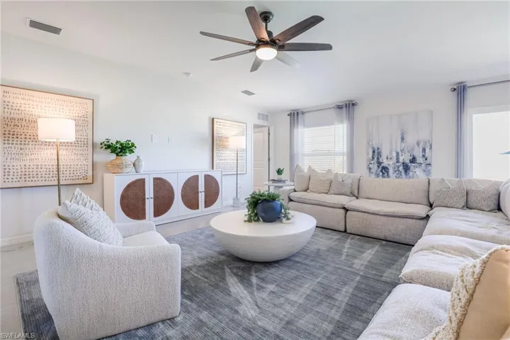 Spacious living area featuring a vaulted ceiling with a ceiling fan, white walls, and large windows with privacy blinds