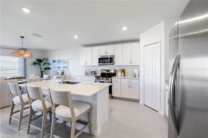 Modern kitchen featuring a large island with sink, white shaker cabinetry, stainless steel appliances, and light-toned tile flooring