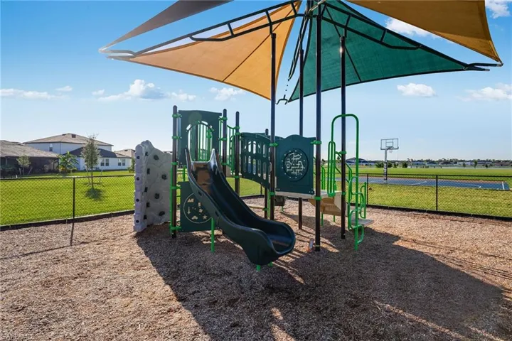 Community playground featuring a multi-level play structure with slides and a climbing wall, sheltered by dual shade canopies