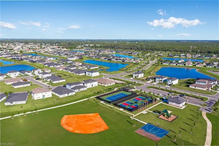 Aerial view of a residential community featuring numerous homes, multiple tranquil ponds, expansive green spaces, an athletic field, and a dedicated sports court area