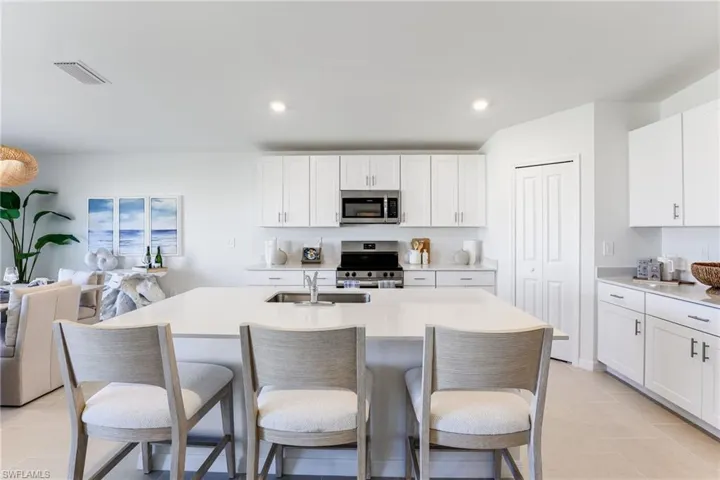 Contemporary kitchen featuring white cabinetry, stainless steel appliances, a large central island with an integrated sink, light-toned countertops, and recessed ceiling lighting