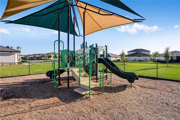 Community playground featuring multiple slides, climbing structures, shade sails, and a wood chip surface