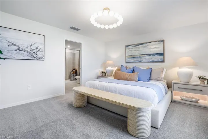 Plush carpeted bedroom featuring a circular ceiling fixture, crisp white walls, and a recessed doorway revealing a bathroom with tile flooring