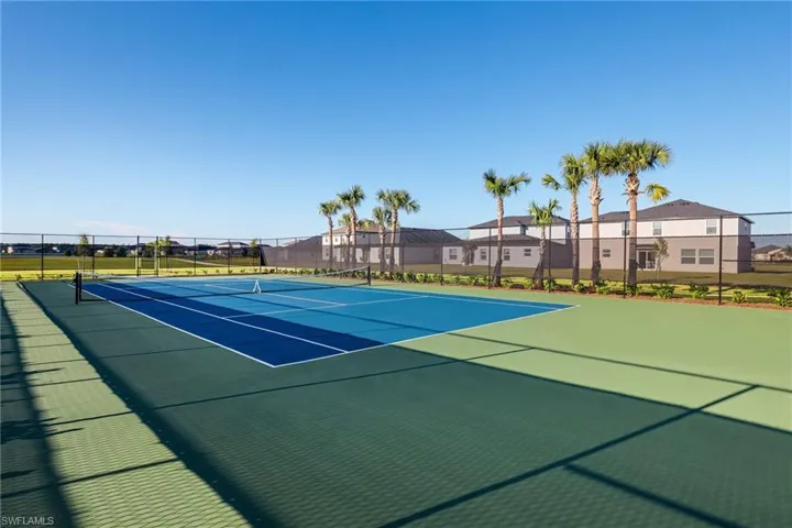 Tennis court featuring a multi-tone blue playing surface with white line markings, surrounded by a black chain-link fence