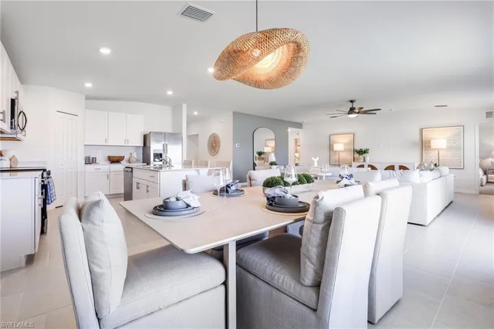 Open-concept living area featuring a dining space with a unique woven pendant light, a kitchen with white cabinetry and stainless steel appliances, and tile flooring throughout