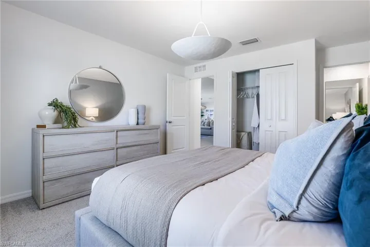 Spacious bedroom featuring light neutral wall tones, plush carpet flooring, a contemporary pendant light fixture, and a bi-fold closet with ample storage