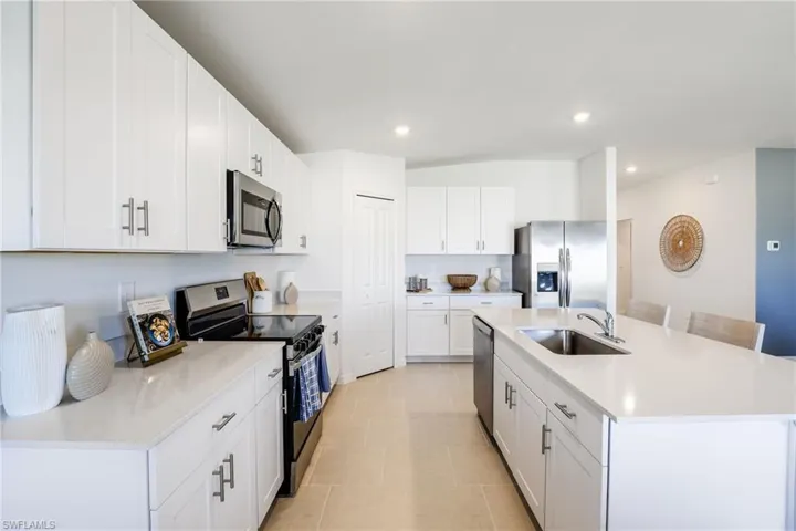 Kitchen with white shaker cabinetry, stainless steel appliances, and a central island featuring an undermount sink and countertop seating