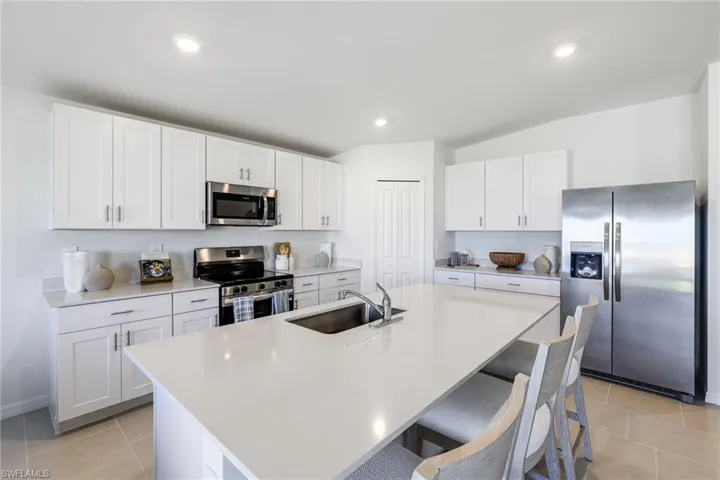 Kitchen featuring a large island with an undermount sink, stainless steel appliances, white shaker-style cabinetry, light countertops, and recessed lighting