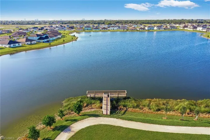 Expansive lakefront setting featuring a wooden dock, a winding path, and manicured green spaces