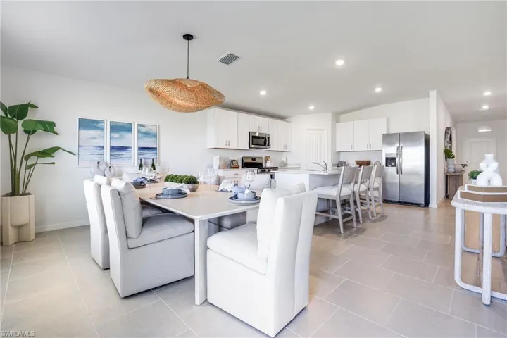 Open-concept kitchen and dining area featuring white cabinetry, stainless steel appliances, a kitchen island with seating, and light-toned tile flooring