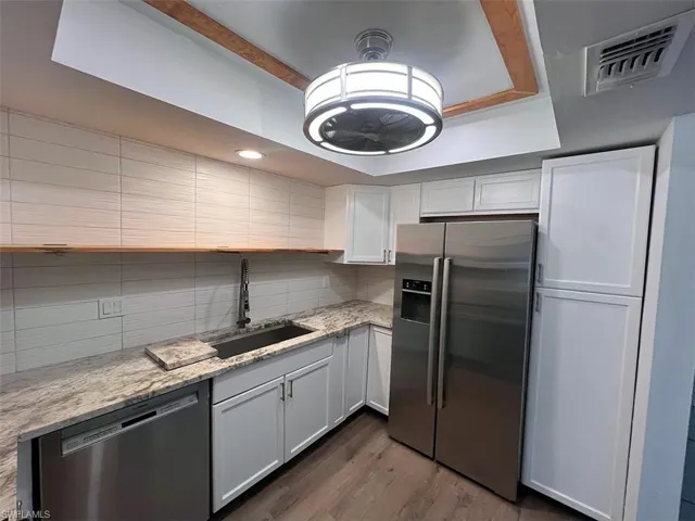 Kitchen featuring stainless steel appliances, light stone counters, dark wood-style flooring, white cabinetry, and backsplash