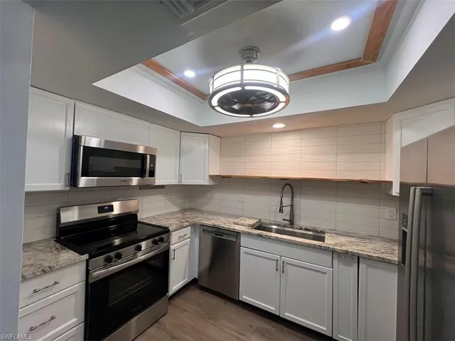 Kitchen with stainless steel appliances, ornamental molding, a raised ceiling, light stone countertops, and dark wood-style flooring